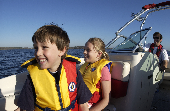 Adult male (dad) wearing an inflatable life jacket at the helm with kids sitting in the bow of an anchored powerboat