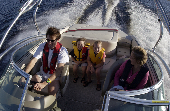 Adult male (dad) and female (mom) wearing inflatable life jackets and kids wearing chidren's life jackets on a moving powerboat.