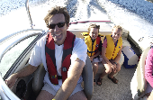 Adult male (dad) wearing an inflatable suspender life jacket driving a motor boat with kids in the back.
