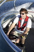 Adult male wearing an inflatable suspender style life jacket driving a motor boat.