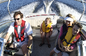 Adult male (dad) wearing an inflatable life jacket driving a motor boat with a boy in a children's life jacket sitting on an adult female's (mom) lap. A girl is is sitting in the back of the boat.