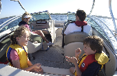 Shot taken from behind the motor boat of an adult male and female and two kids (boy and girl)