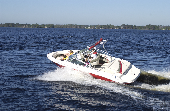 Adult male (dad) and adult female (mom) on a motor boat. Two children (boy and girl) are sitting in the bow. Trees are in the background.
