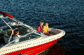 Adult female wearing an inflatable life jacket and a girl in a children's life jacket  sitting in the bow, while an adult male is behind the wheel