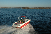 Adult male and female along with boy and girl in a moving motor boat with the shoreline in the background.