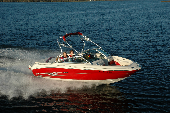 Adult male and female along with boy and girl in a moving motor boat with the shoreline in the background.