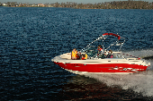Adult male and female along with boy and girl in a moving motor boat with the shoreline in the background.