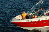 Adult male wearing an inflatable life jacket driving a motor boat, with a boy and girl wearing children's life jackets sitting in the bow.
