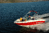 Adult male and female wearing inflatable life  jackets with a boy and girl wearing children's life jackets sitting in the bow of a moving motor boat. The shoreline is in the background.