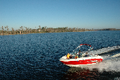 Adult male and female wearing inflatable life jackets with a boy and girl wearing children's life jackets sitting in the bow of a moving motor boat. The shoreline is in the background.