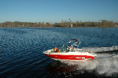 Adult male and female wearing inflatable life jackets with a boy and girl wearing children's life jackets sitting in the bow of a moving motor boat. The shoreline is in the background.